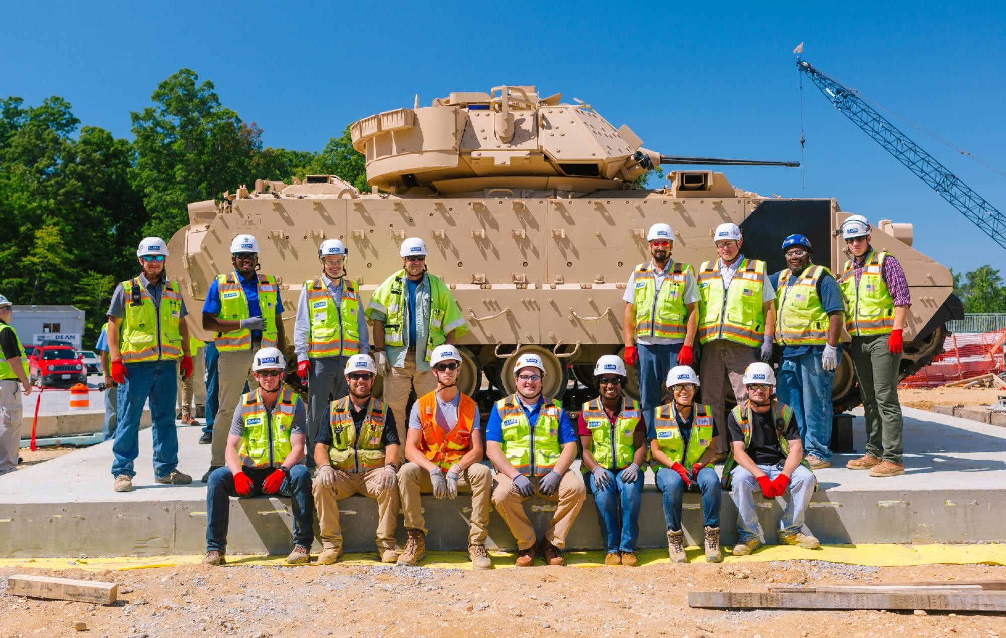 Construction crew in branded safety vests and hard hats in front of a military vehicle